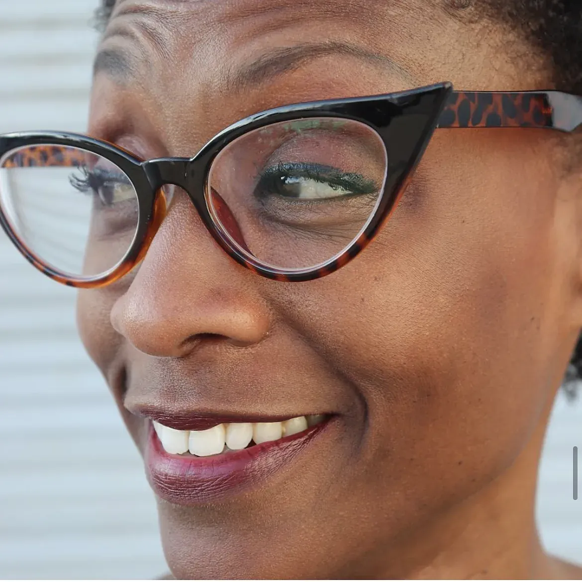 An actor in cat-eye glasses smiles off camera