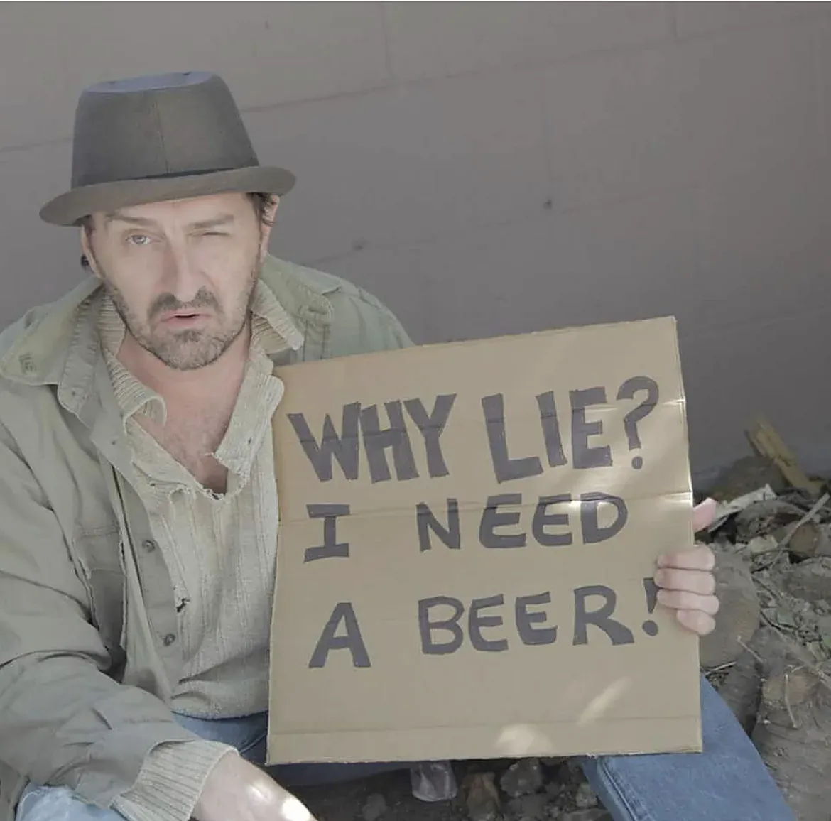 An actor winks while holding a sign that reads "Why lie? I need a beer!"