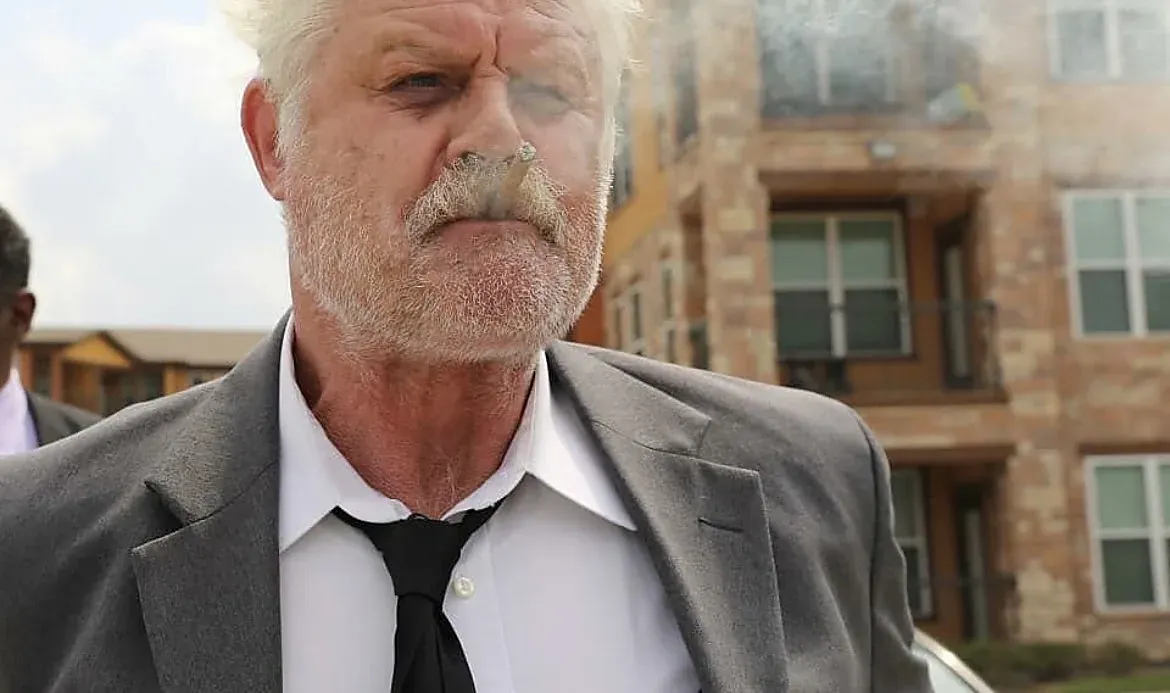 An actor in a gray suit and tie with a cigar